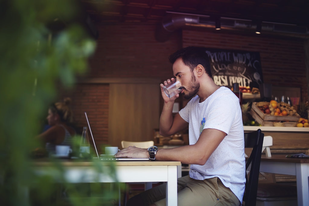 رجل يعمل على جهاز كمبيوتر ويحتسي القهوة في مطعم