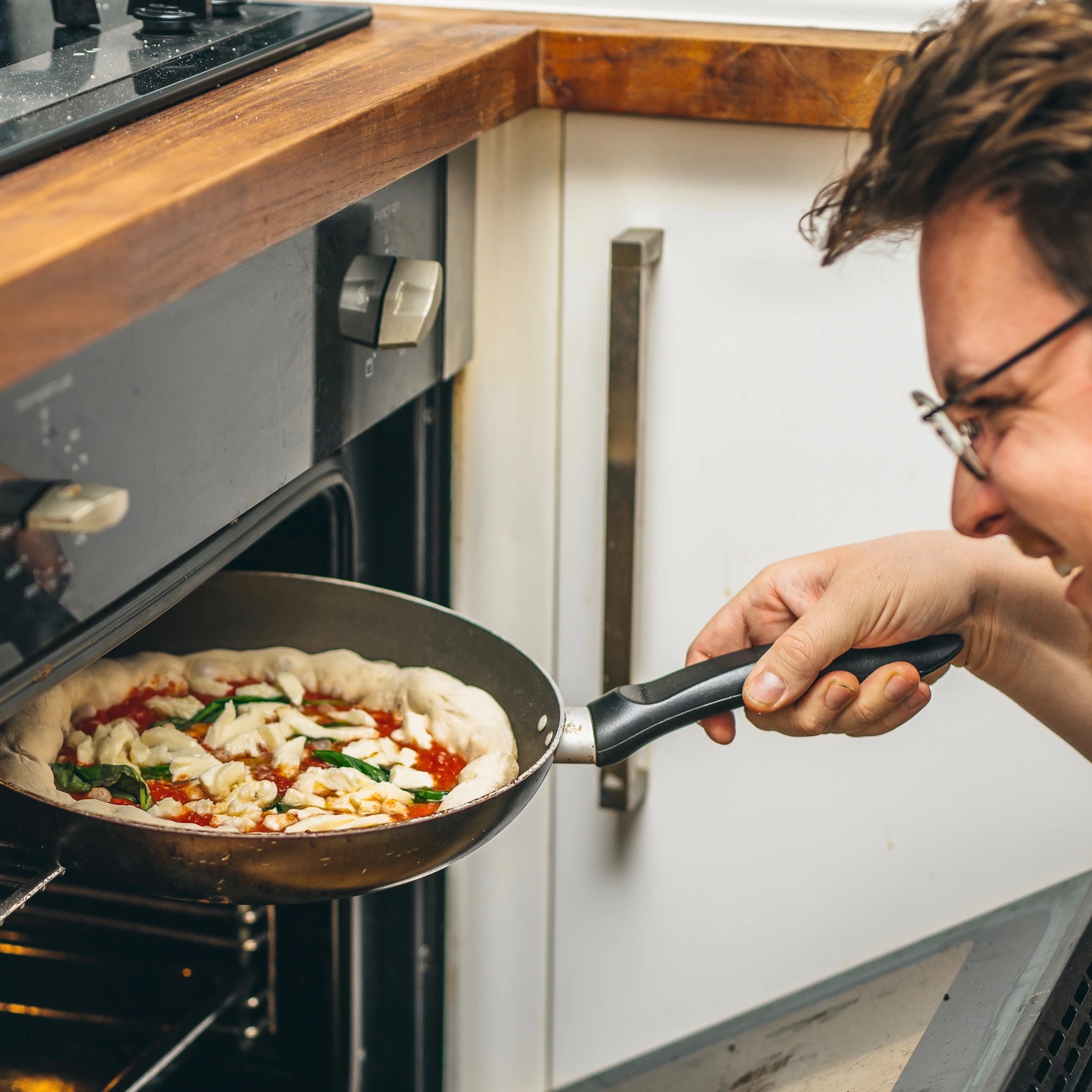 James Elliot demostrando cómo hacer una pizza con sus kits de pizza, una sartén y un horno.