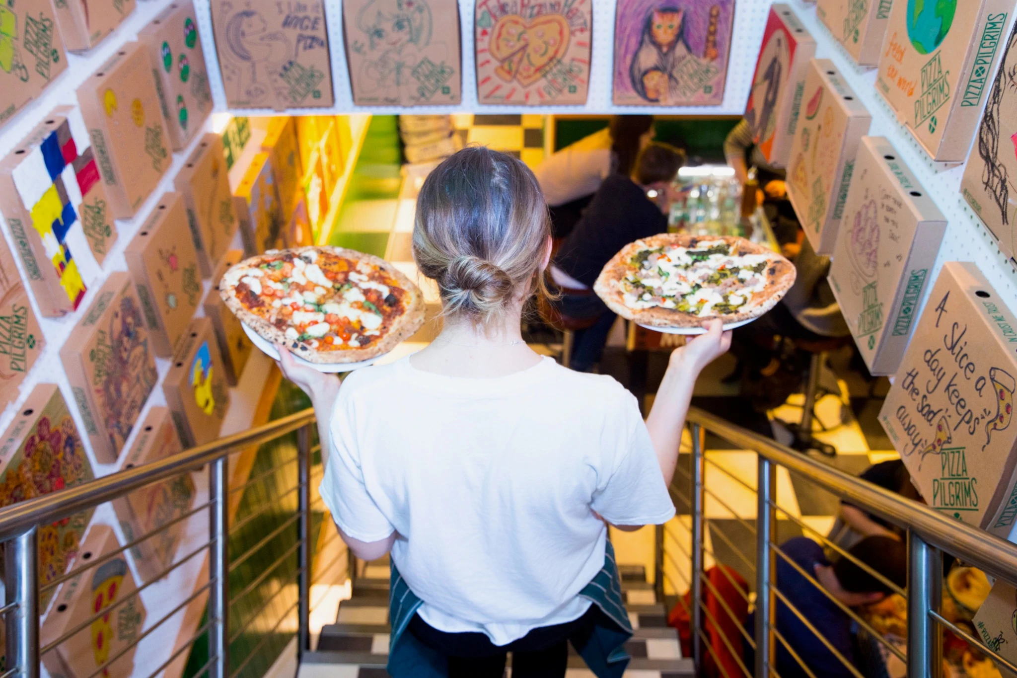 Una camarera con dos pizzas en las manos en la ubicación de Pizza Pilgrims en Shoreditch en sus bulliciosos días antes de COVID-19