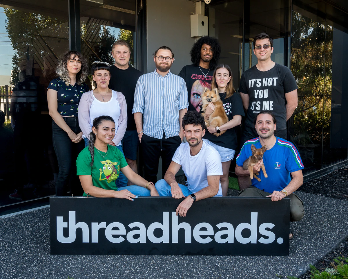 El equipo detrás de Threadheads frente a su oficina con un cartel de Threadheads frente al grupo.