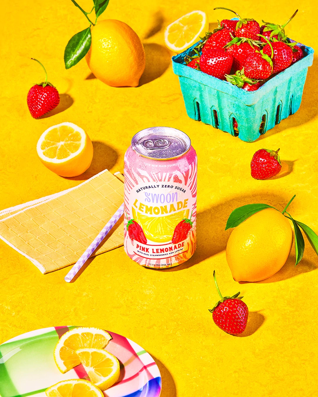 علبة عصير ليمون وردي من Swoon على خلفية صفراء مع الفراولة والليمون في الإطار.