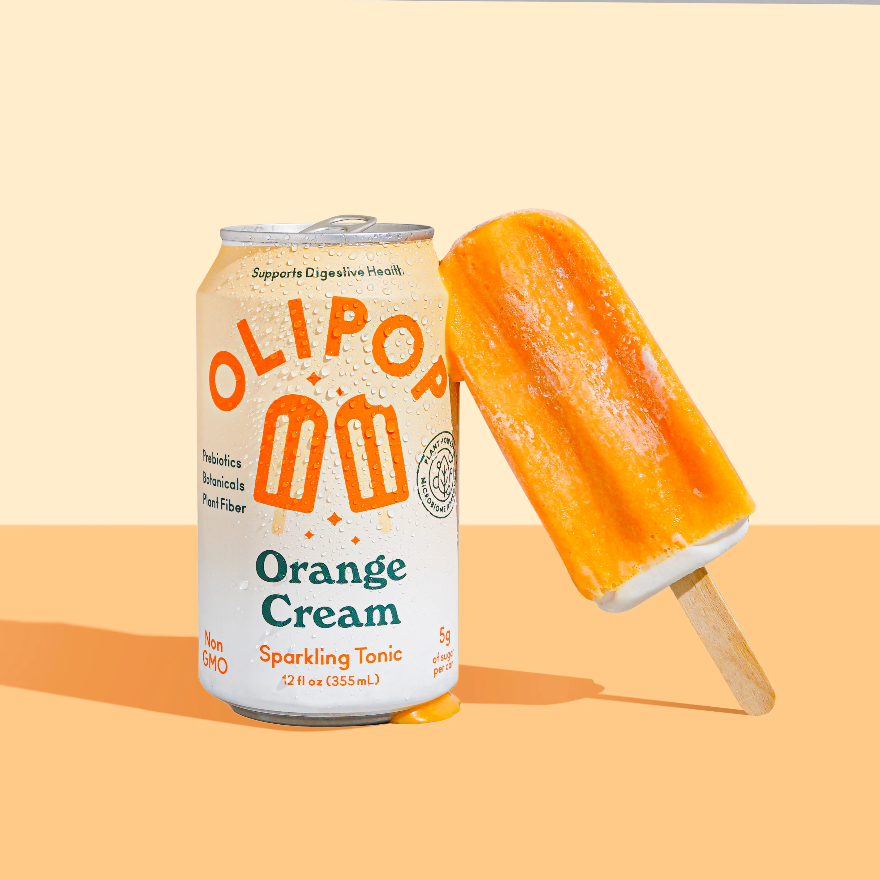 O cutie de olipop cu cremă de portocale cu un popsicle sprijinit de ea, pe fundal portocaliu deschis.