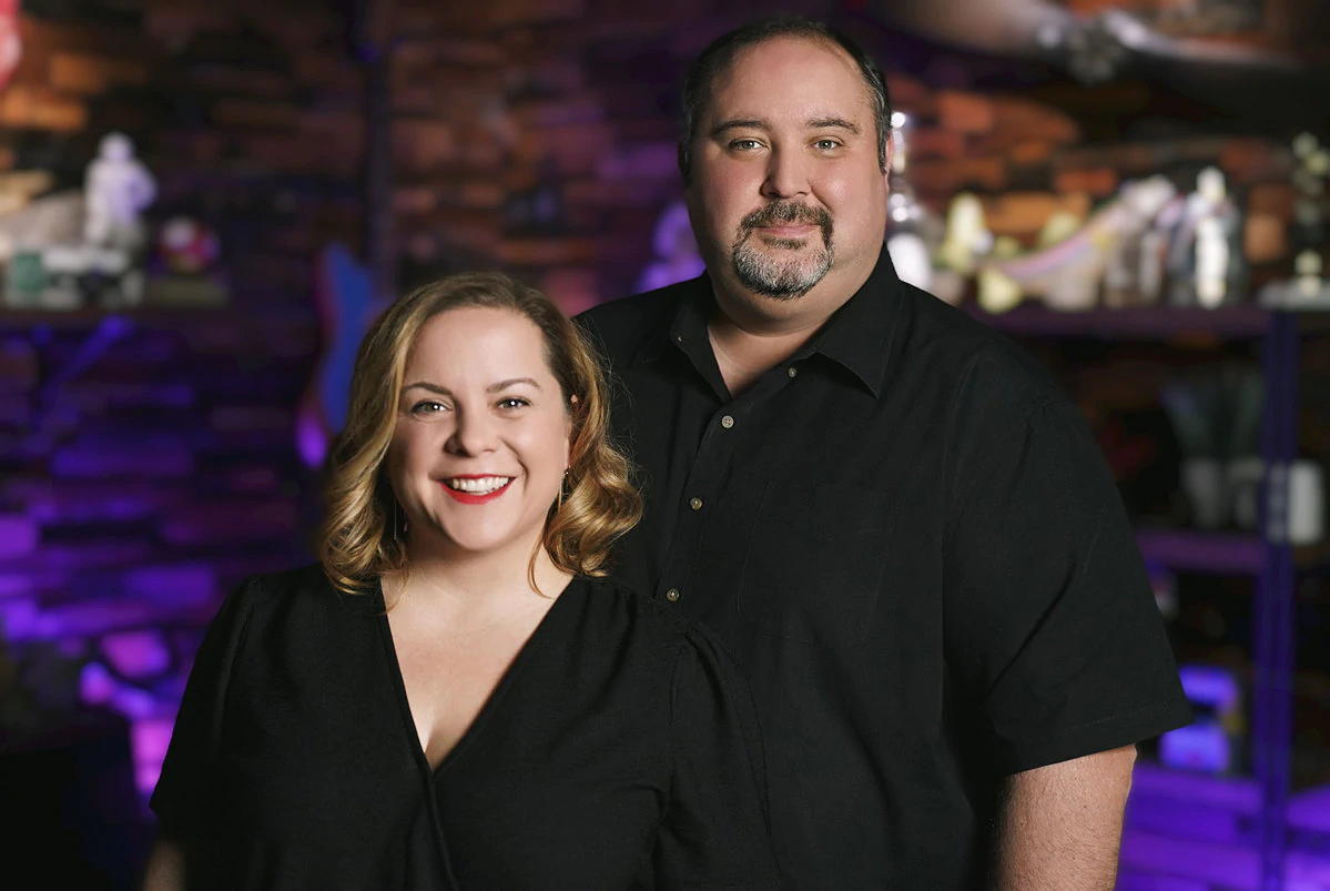 John Ruggiero et Michelle Luchese, les cofondateurs des groupes Manly, portent tous deux du noir dans un salon sombre et flou.